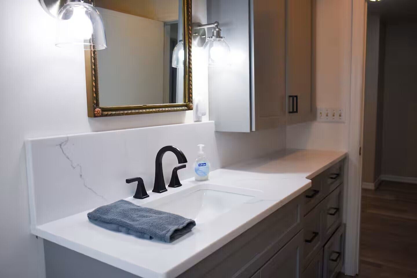 Un baño con un lavamanos blanco, grifo negro y una toalla sobre la encimera.