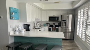 A modern kitchen with white cabinets, stainless steel appliances, a teal island with bar stools, and a blue wall decoration. - Beautiful island escape in beach community (Fort Pierce)