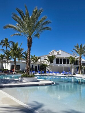 A pool area with palm trees, lounge chairs, and a building with large windows. - Beautiful island escape in beach community (Fort Pierce)
