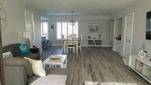 A spacious living area with a grey sofa, a dining table with chairs, and a kitchen area with cabinets and a TV. - Beautiful island escape in beach community (Fort Pierce)
