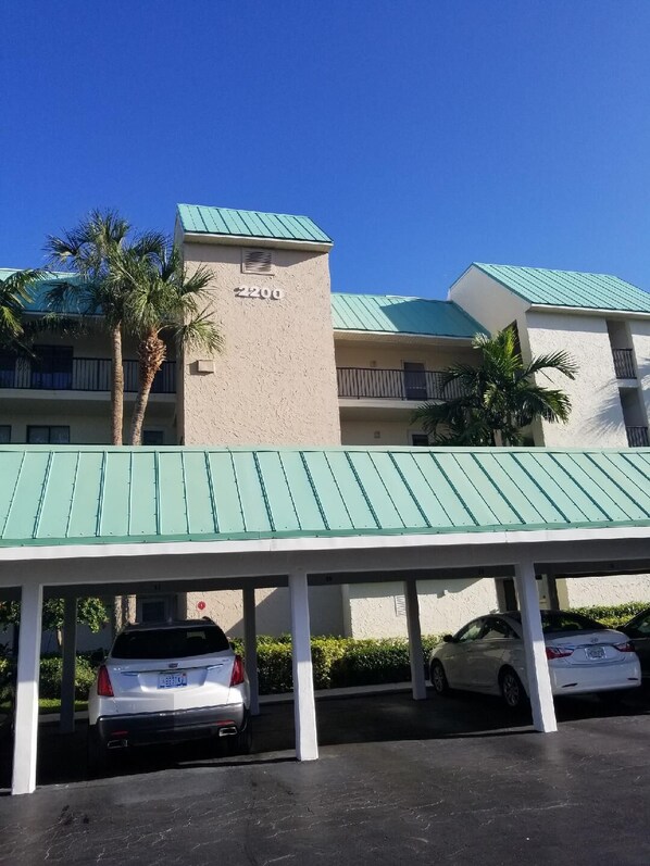 A building with a beige facade and green roof, featuring a parking area with several cars. - Beautiful island escape in beach community (Fort Pierce)