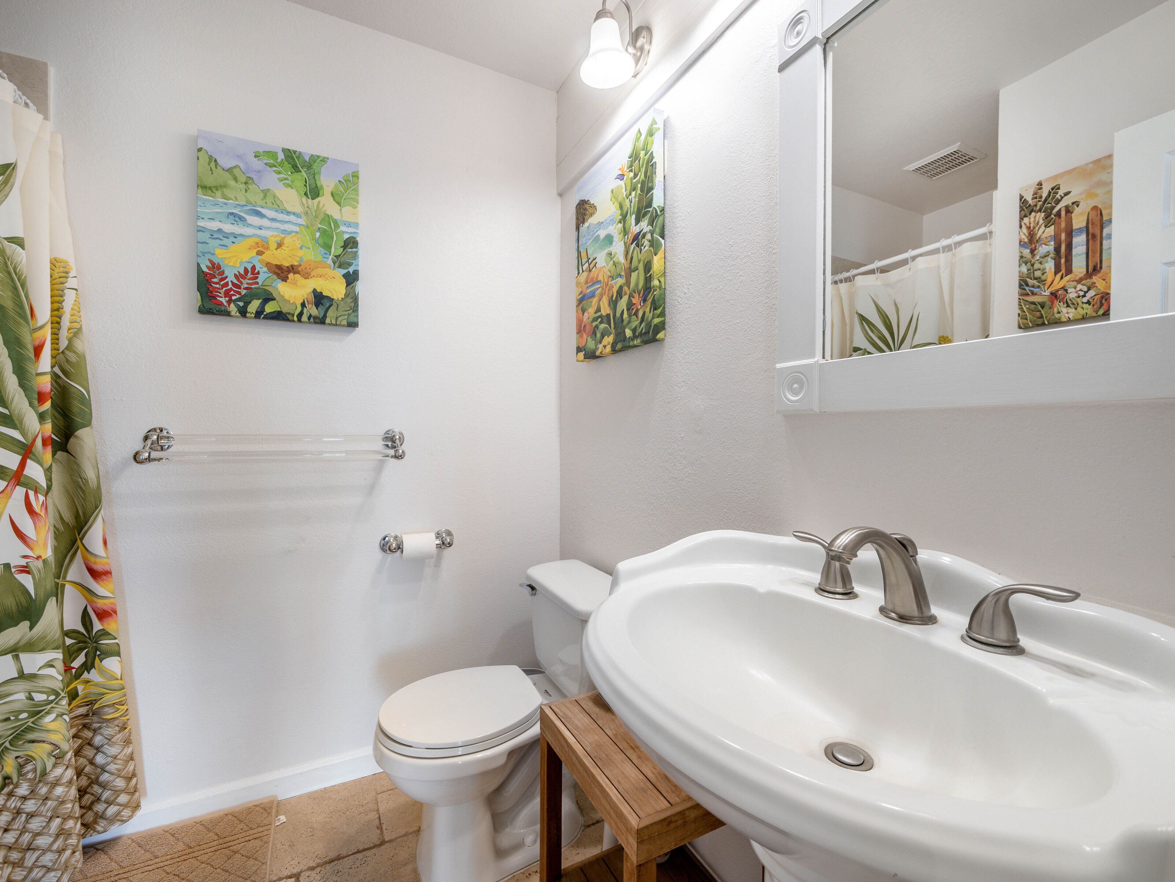 A bathroom with a toilet, sink, and two wall-mounted paintings.