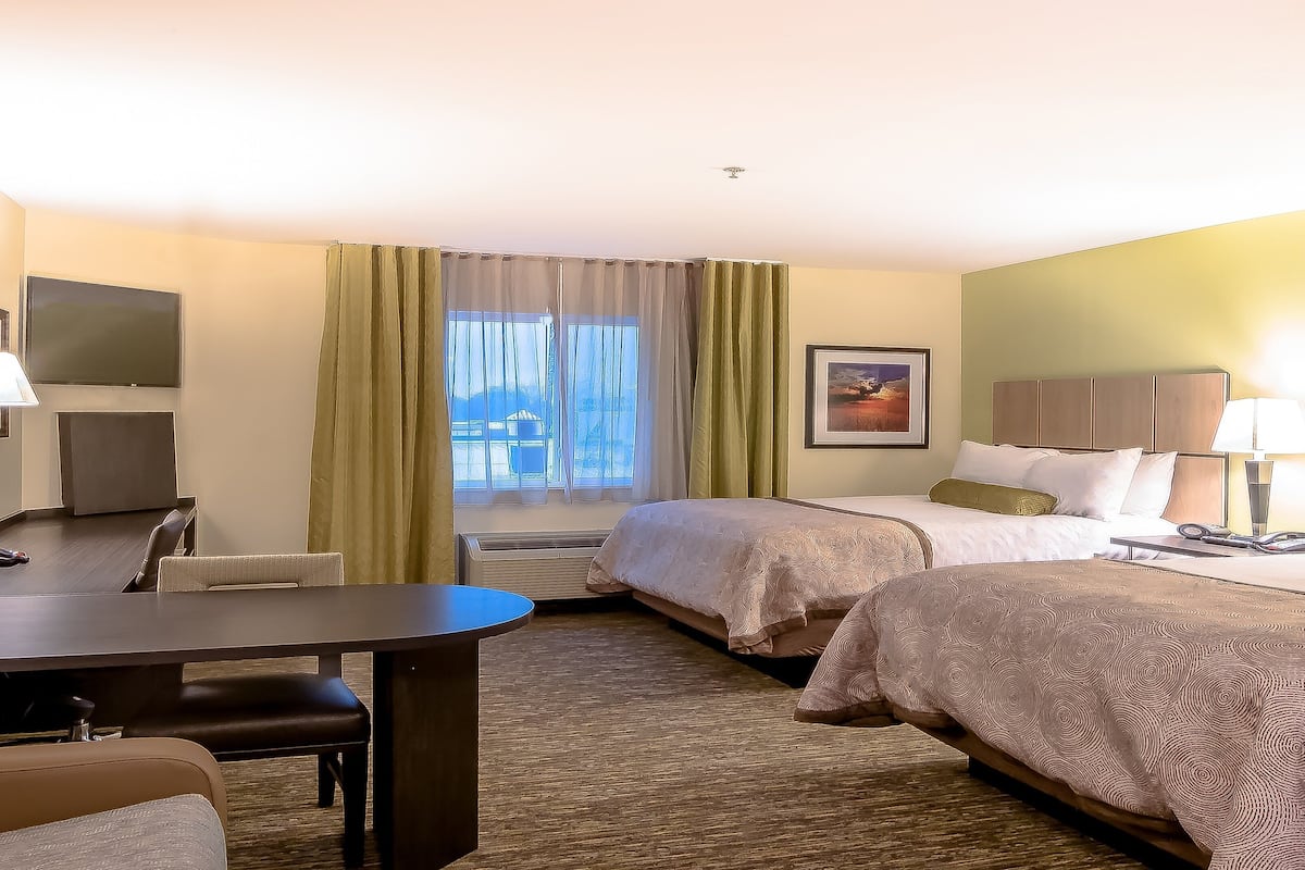 Quarto de hotel com duas camas, uma escrivaninha, uma cadeira, uma televisão e uma janela com cortinas.