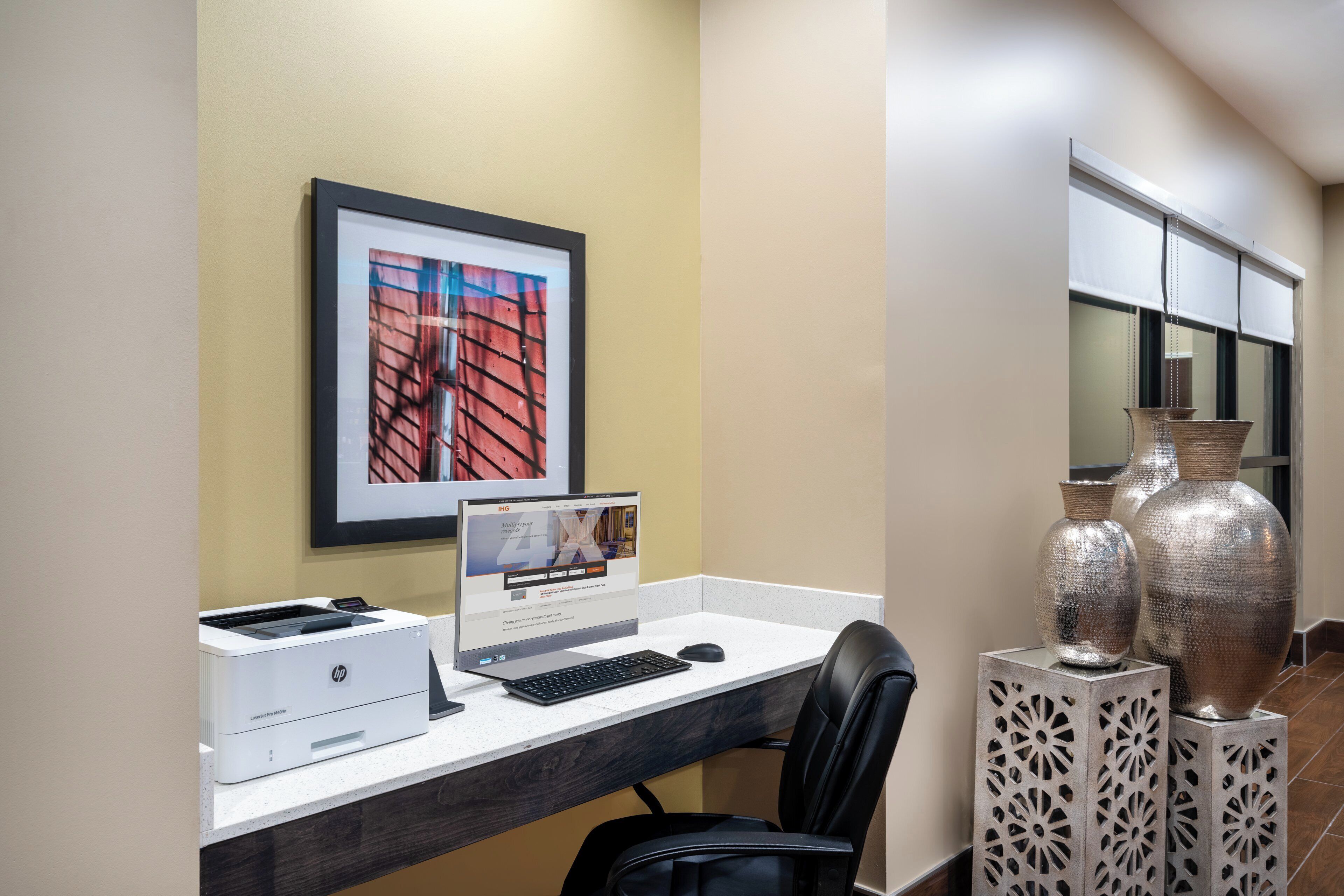 A hotel workspace with a desktop computer, printer, and a framed picture on the wall.