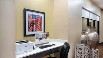 A hotel workspace with a desktop computer, printer, and a framed picture on the wall.