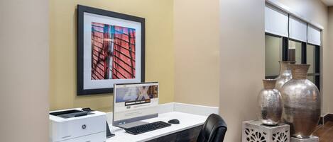 A hotel workspace with a desktop computer, printer, and a framed picture on the wall.