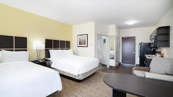 A hotel room with two beds, a desk, a chair, a small kitchenette, and a bathroom.