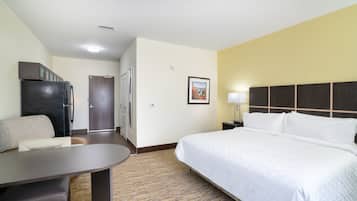 A hotel room with a bed, a desk, a refrigerator, and a door leading to a bathroom.
