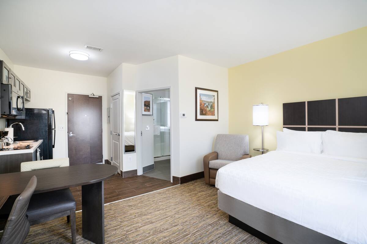 Quarto de hotel com cama, escrivaninha, cadeira, abajur e um quadro na parede.
