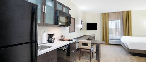 A compact hotel room with a kitchenette, a dining area, a bed, and a TV.