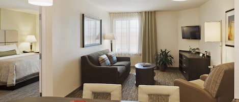 A hotel room with a bed, a sofa, a dining table with placemats, a television, and a plant.