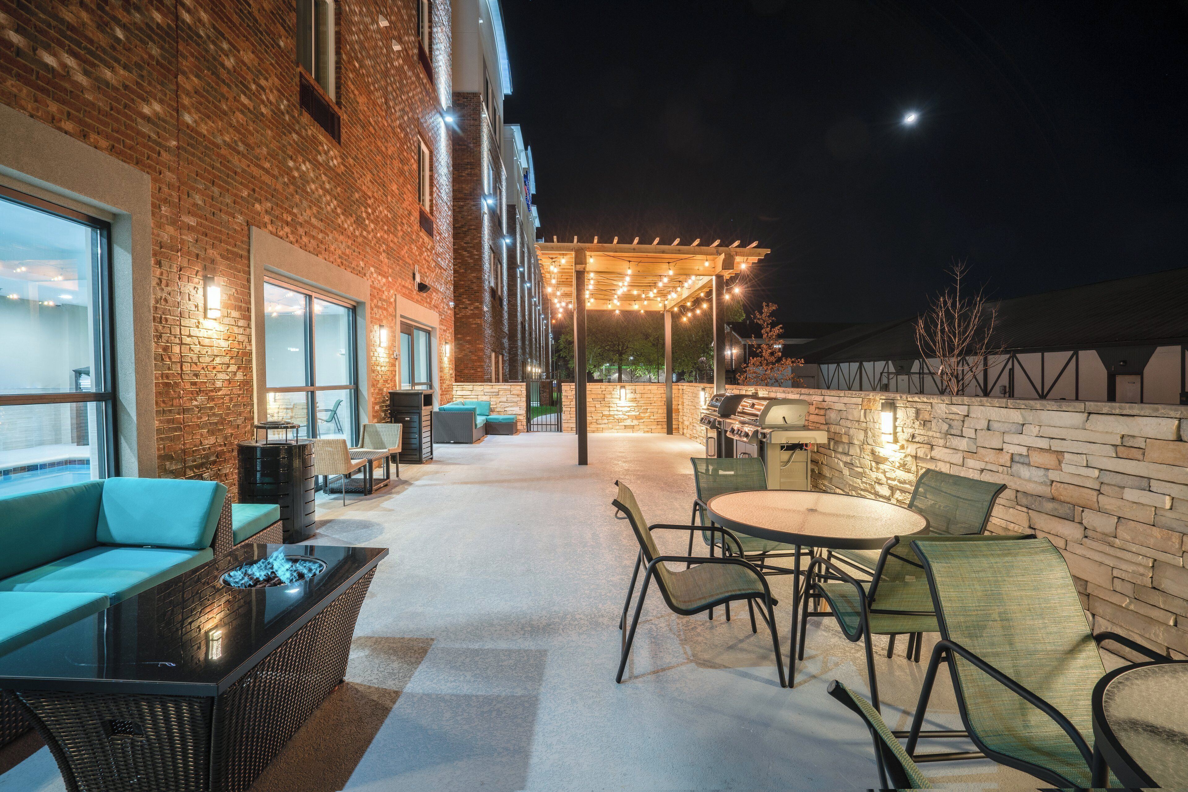An outdoor patio area with brick walls, a seating area with a fire feature, and a grill station.