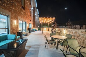 Un espace extérieur aménagé en patio, avec des murs en briques, un coin salon doté d’un foyer et un espace barbecue.