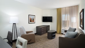 A hotel room with a flat-screen TV, two sofas, a small table, a lamp, a cabinet, and a large window with curtains. - Candlewood Suites Nashville - Franklin by IHG (Franklin)