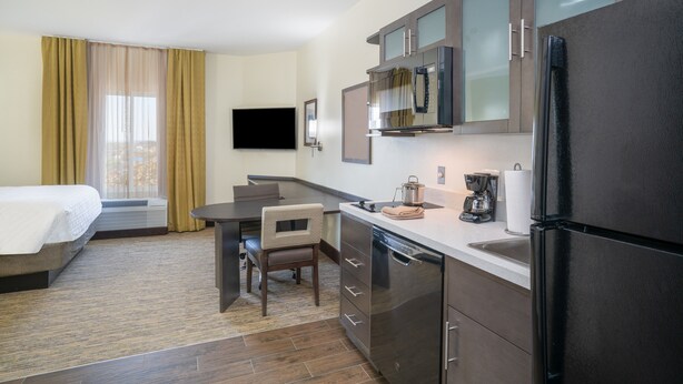 A hotel room with a bed, a desk, a chair, a kitchen area with a refrigerator, microwave, and a coffee maker. - Candlewood Suites Nashville - Franklin by IHG (Franklin)