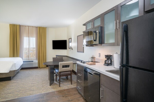 Une chambre d’hôtel équipée d’un lit, d’un bureau, d’une chaise et d’un coin cuisine comprenant un réfrigérateur, un four à micro-ondes et une machine à café.