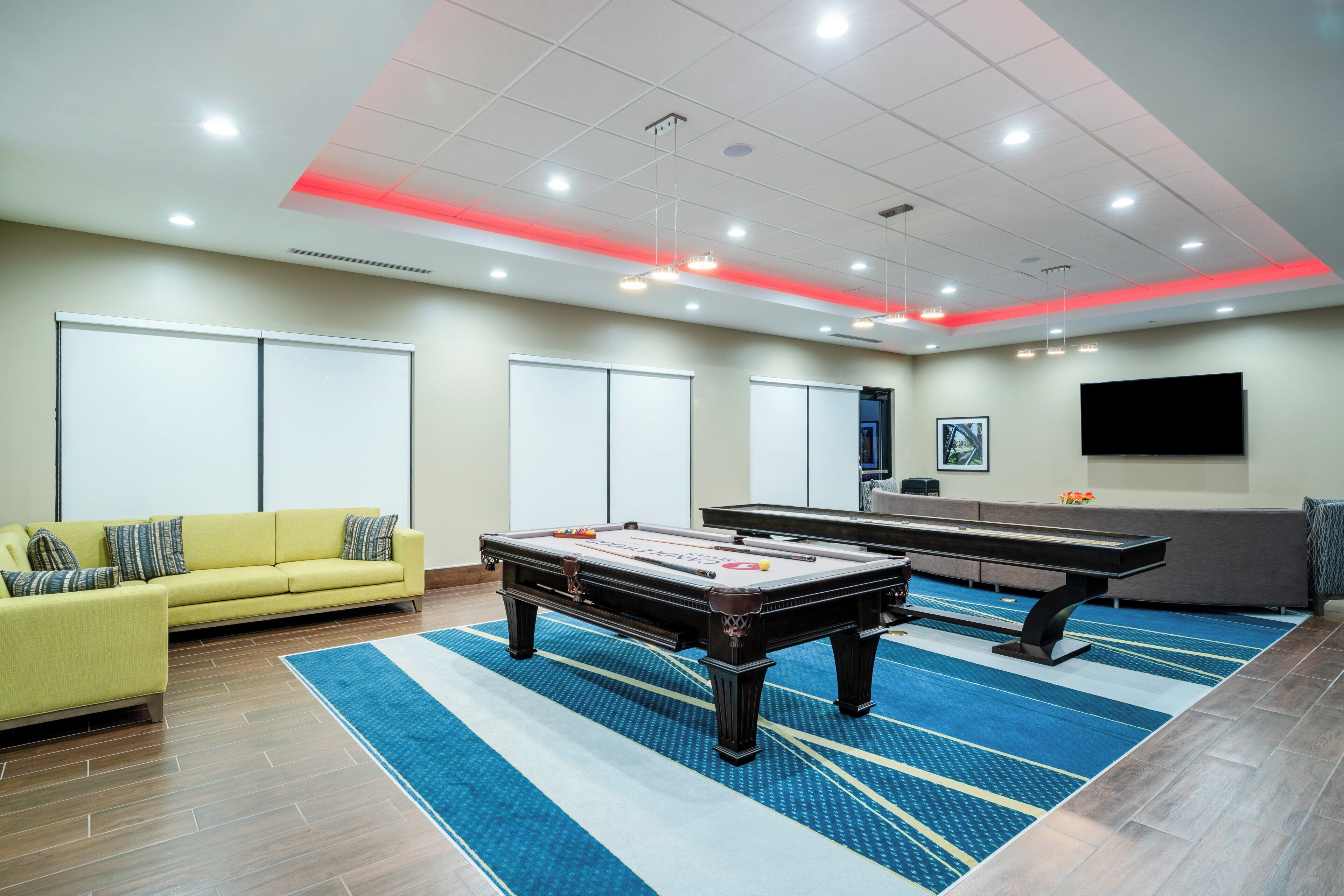A room with a pool table, a yellow sofa, and a large flat-screen TV mounted on the wall.