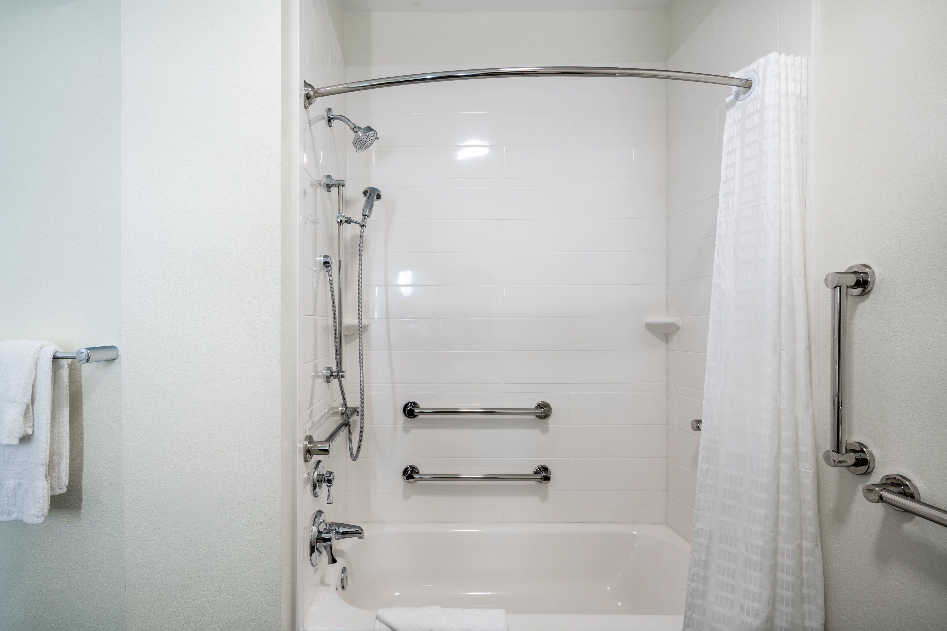 Ein helles Badezimmer mit einer Badewanne, einer Dusche mit Glastür und zwei Haltegriffen.