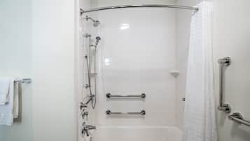 A white bathroom with a bathtub, a shower with a glass door, and two handrails.