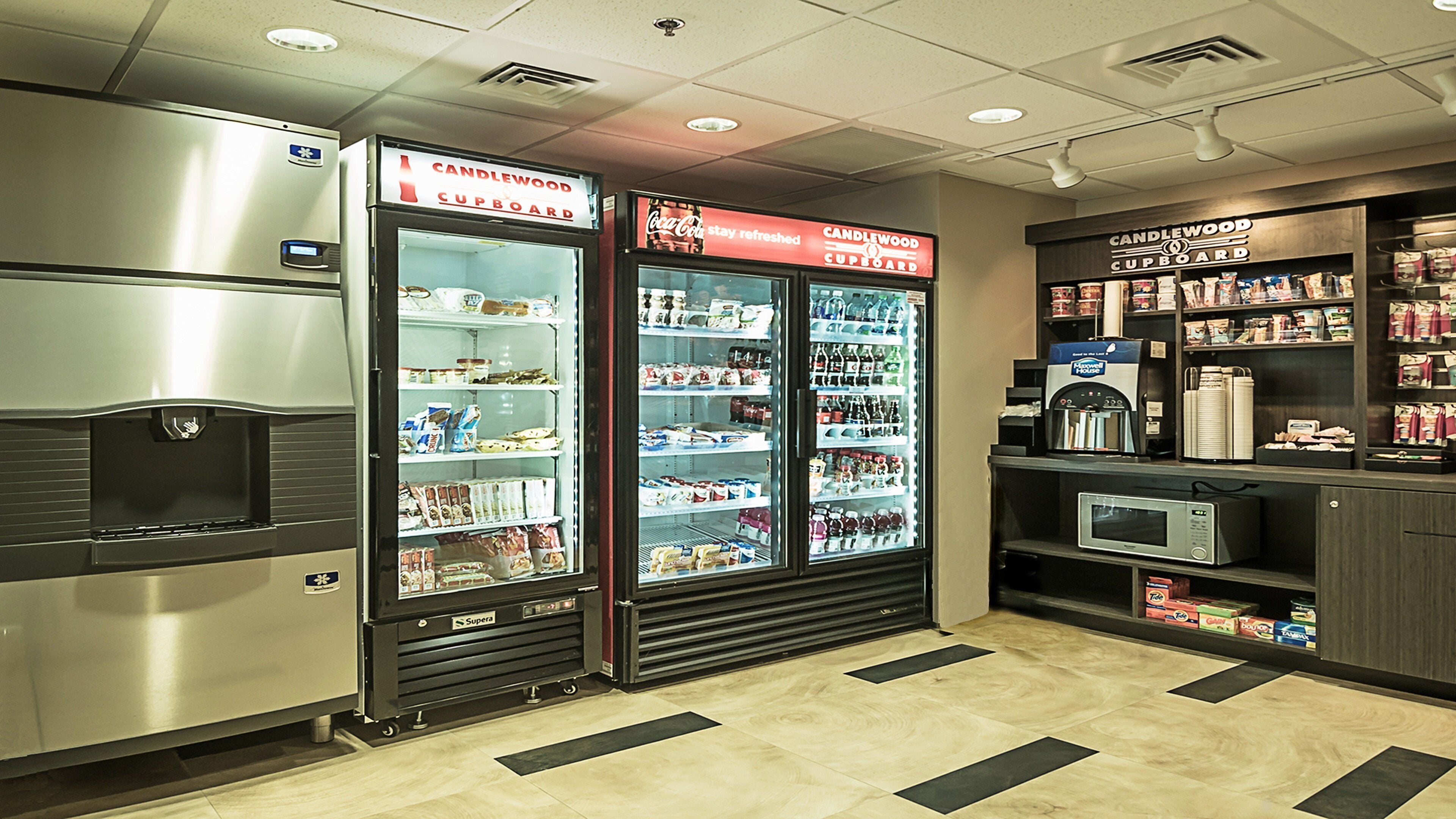 Un área de autoservicio con dispensadores de bebidas refrigeradas, microondas y una selección de bocadillos y bebidas.