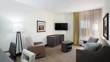 A hotel room with a sofa, armchair, desk, lamp, TV, and a painting on the wall.
