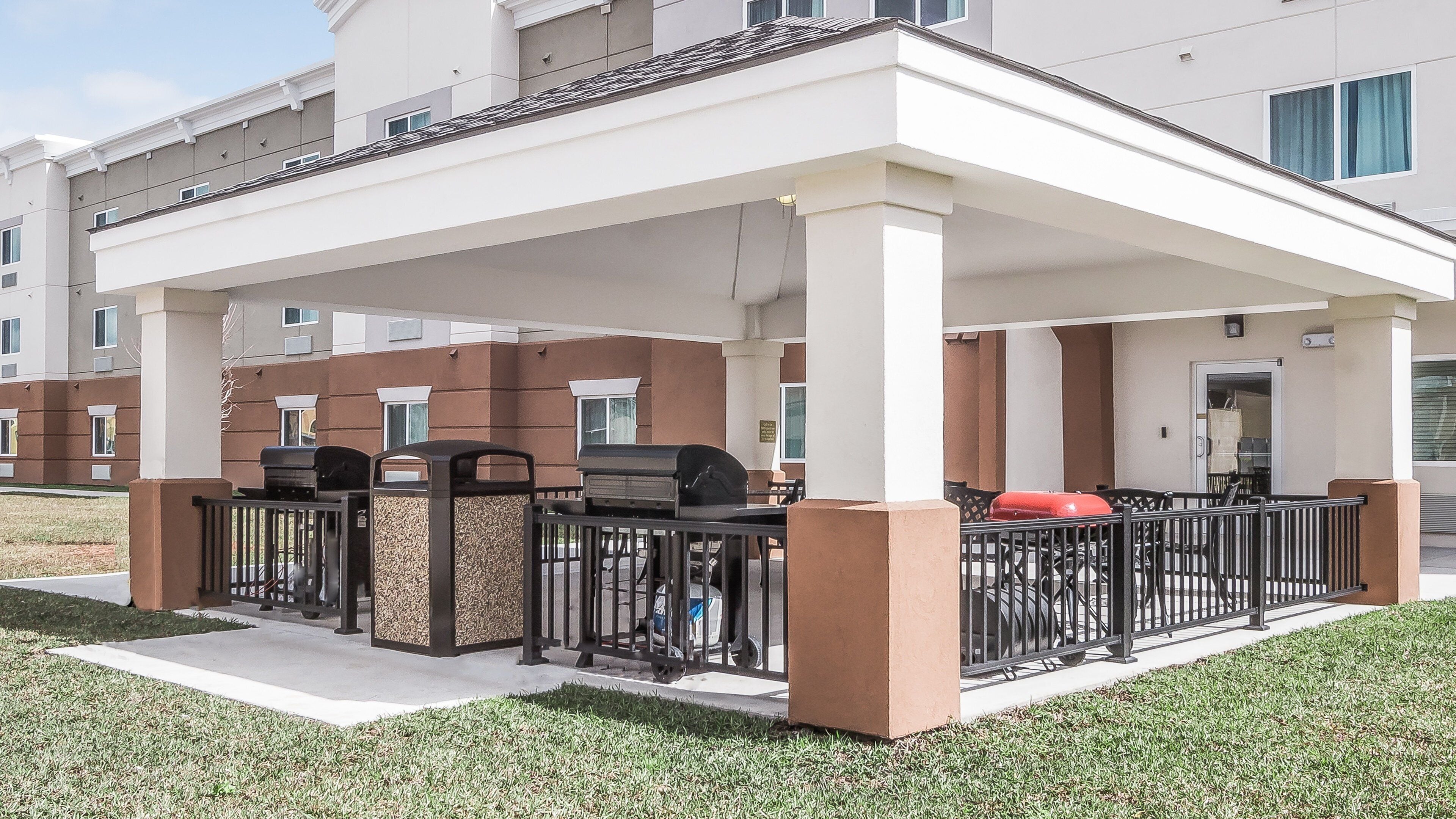 A covered outdoor area with barbecue grills, a trash bin, and a red object on the ground.