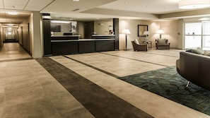 Un hall de hotel con una recepción, una zona de estar con un sofá y sillones, y una alfombra estampada.