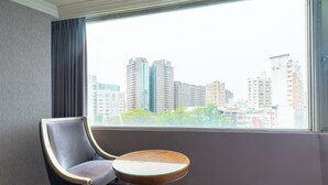 Hotellihuone, jossa on suuri ikkuna, tuoli ja pieni pöytä.