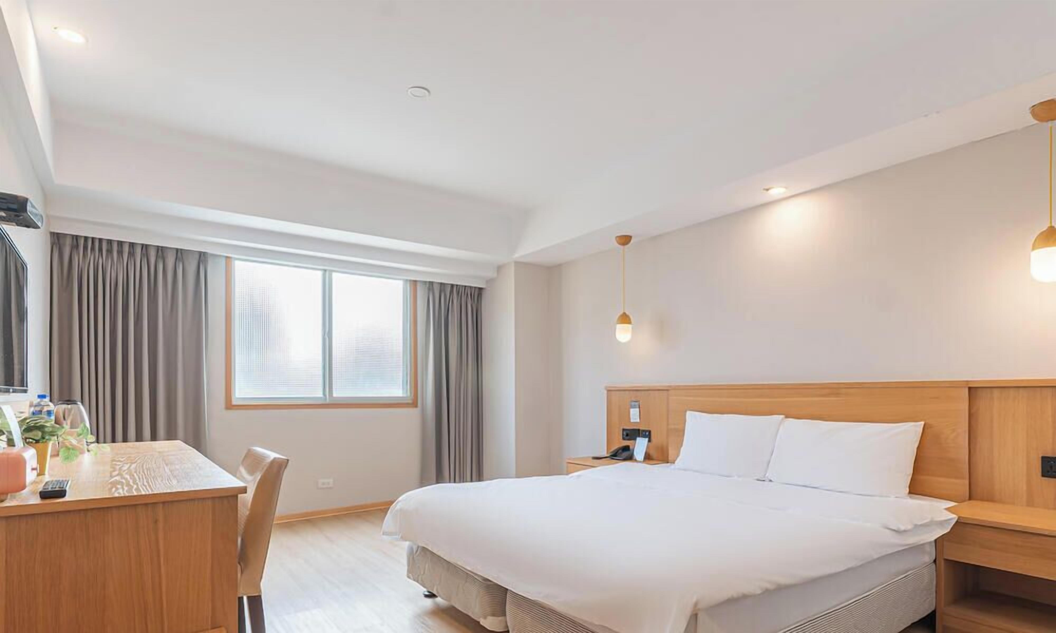 A hotel room with a large bed, bedside table, and a desk with a chair.