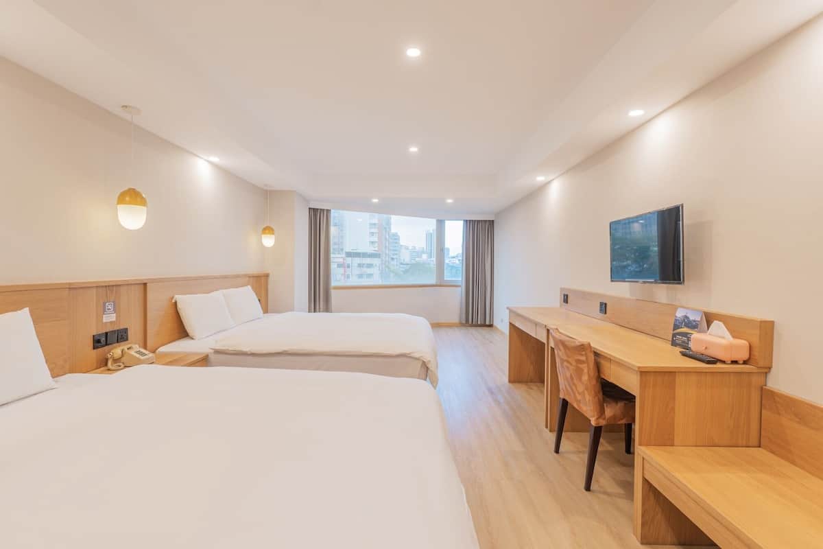 A hotel room with two beds, a desk, a chair, a TV, and a window with a city view.