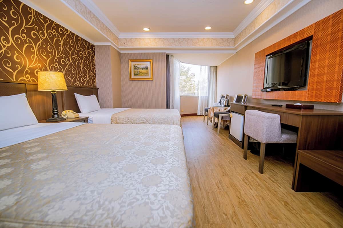A hotel room with two beds, a desk with a chair, a television, and a window with curtains.