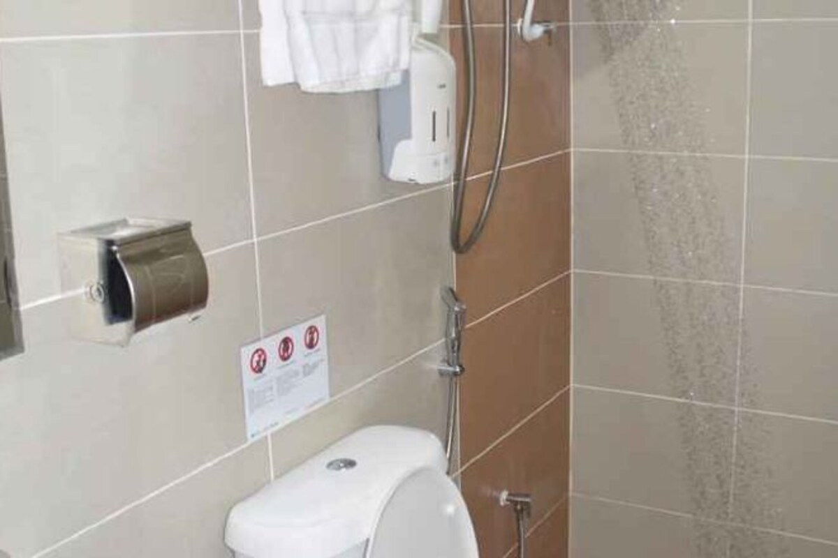 Casa de banho com sanita, dispensador de papel, dispensador de sabonete e chuveiro.