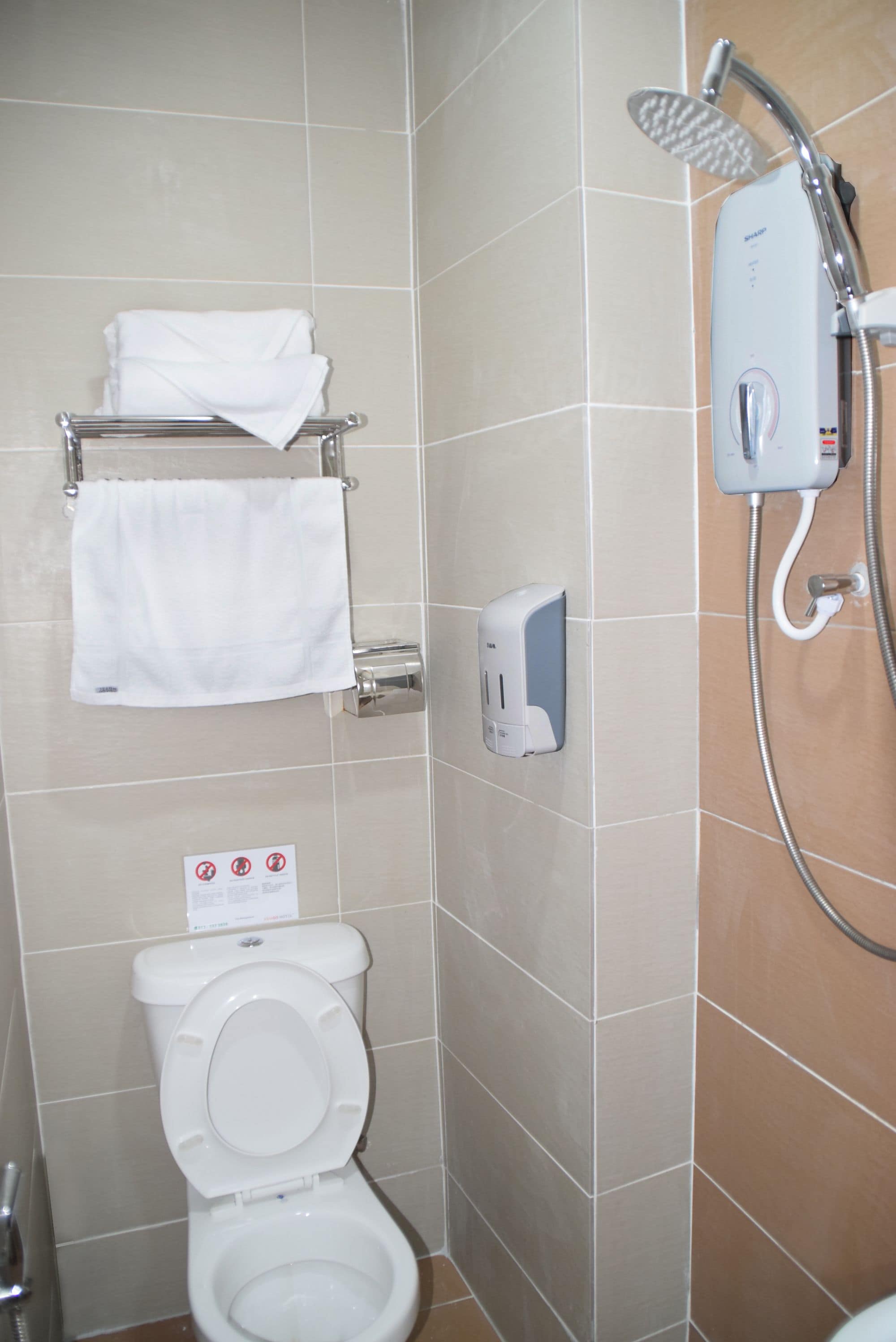 Casa de banho com sanita, um porta-toalhas com uma toalha dobrada, dispensador de sabonete e chuveiro.