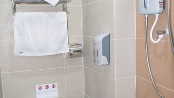 Casa de banho com sanita, um porta-toalhas com uma toalha dobrada, dispensador de sabonete e chuveiro.