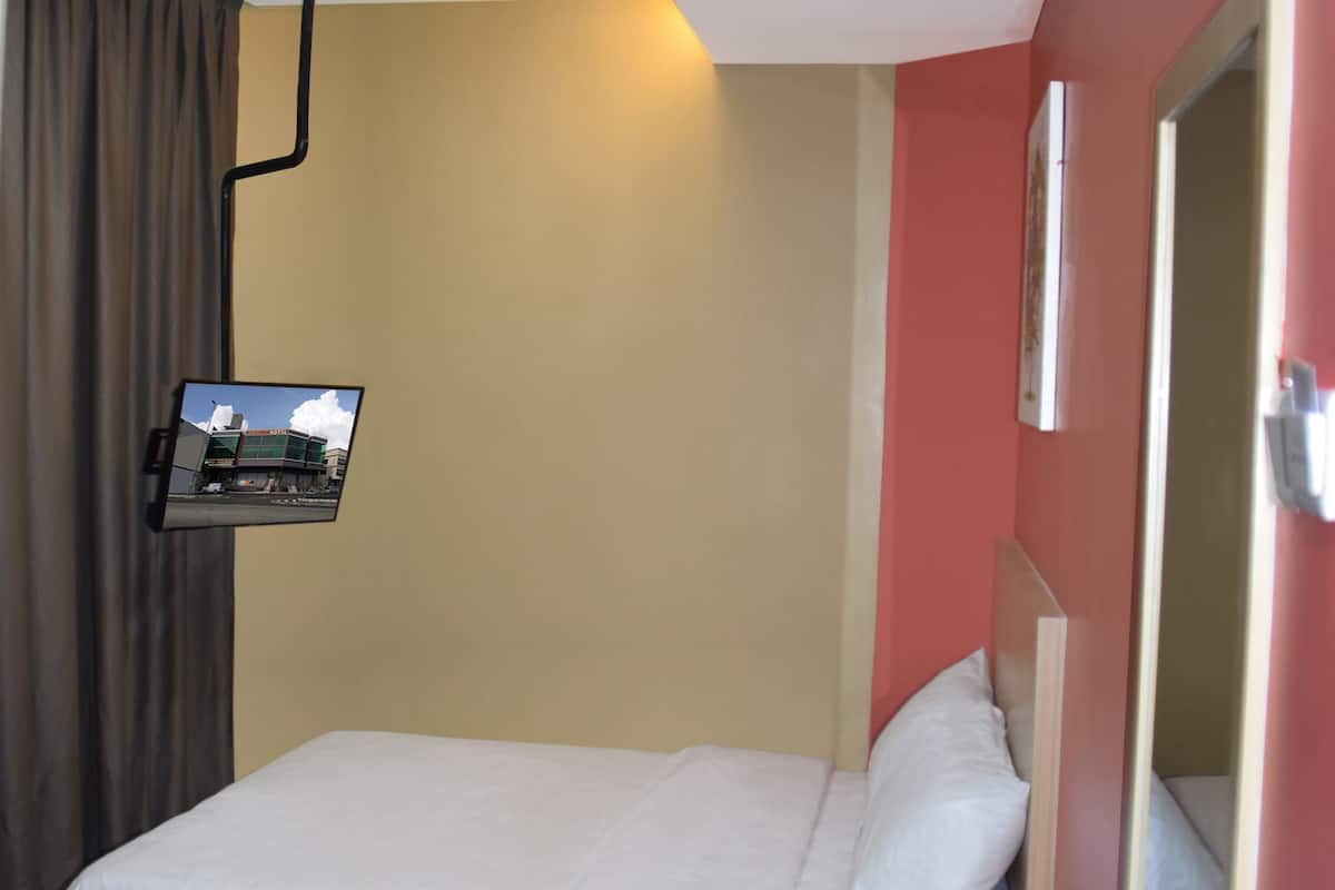Une chambre d’hôtel avec un lit, un téléviseur fixé au mur, un miroir et une porte.