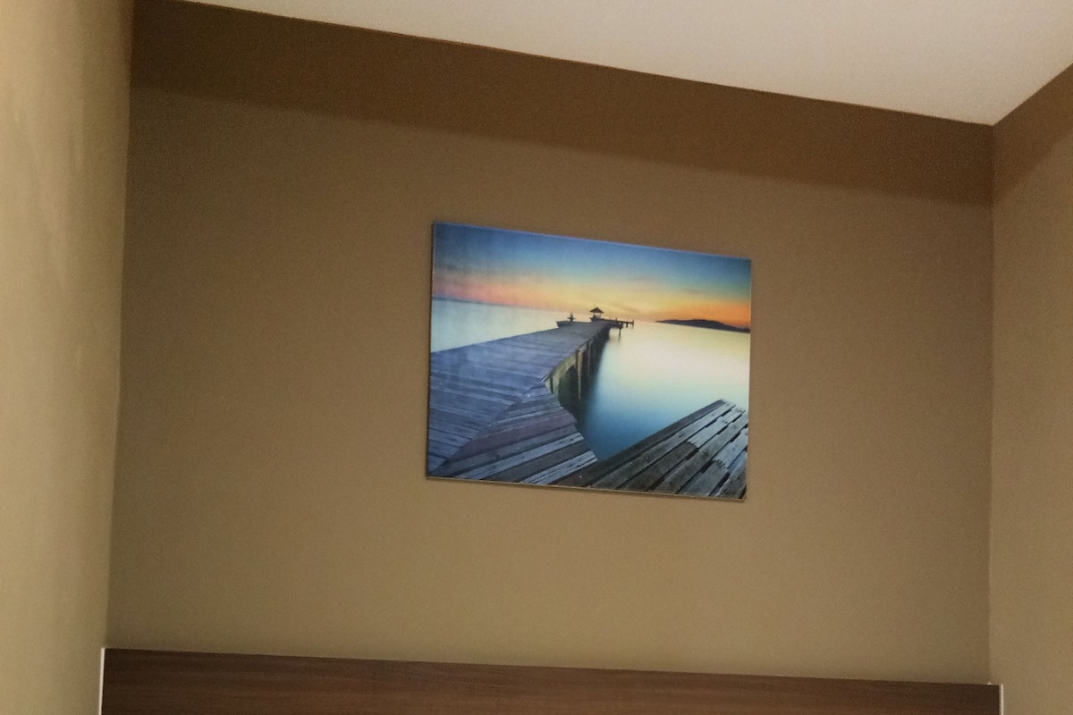 Une chambre d’hôtel avec un lit, une table de chevet et un tableau représentant un coucher de soleil sur l’eau, accroché au mur.