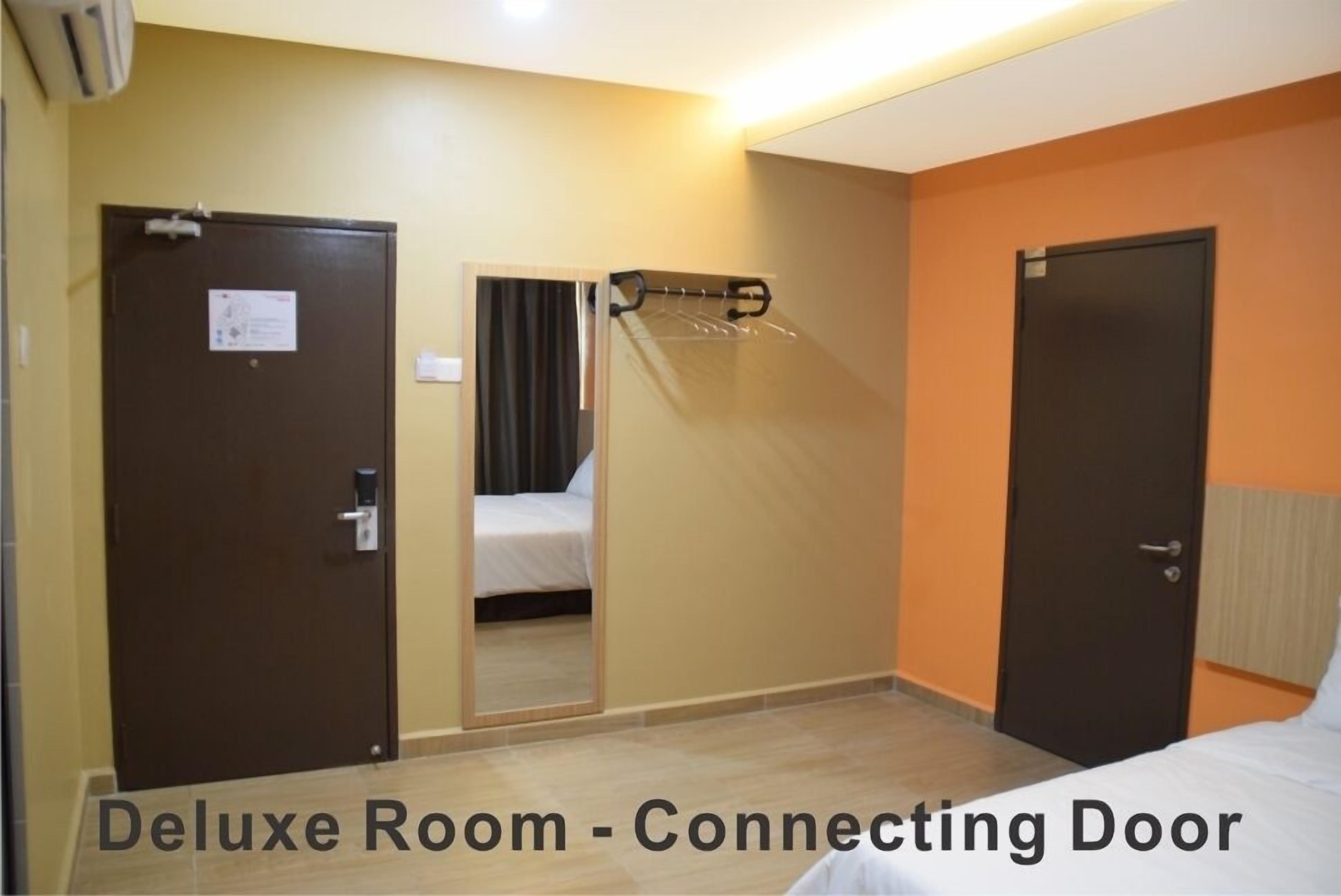A deluxe room with a connecting door, a bed, a mirror, and a coat rack.