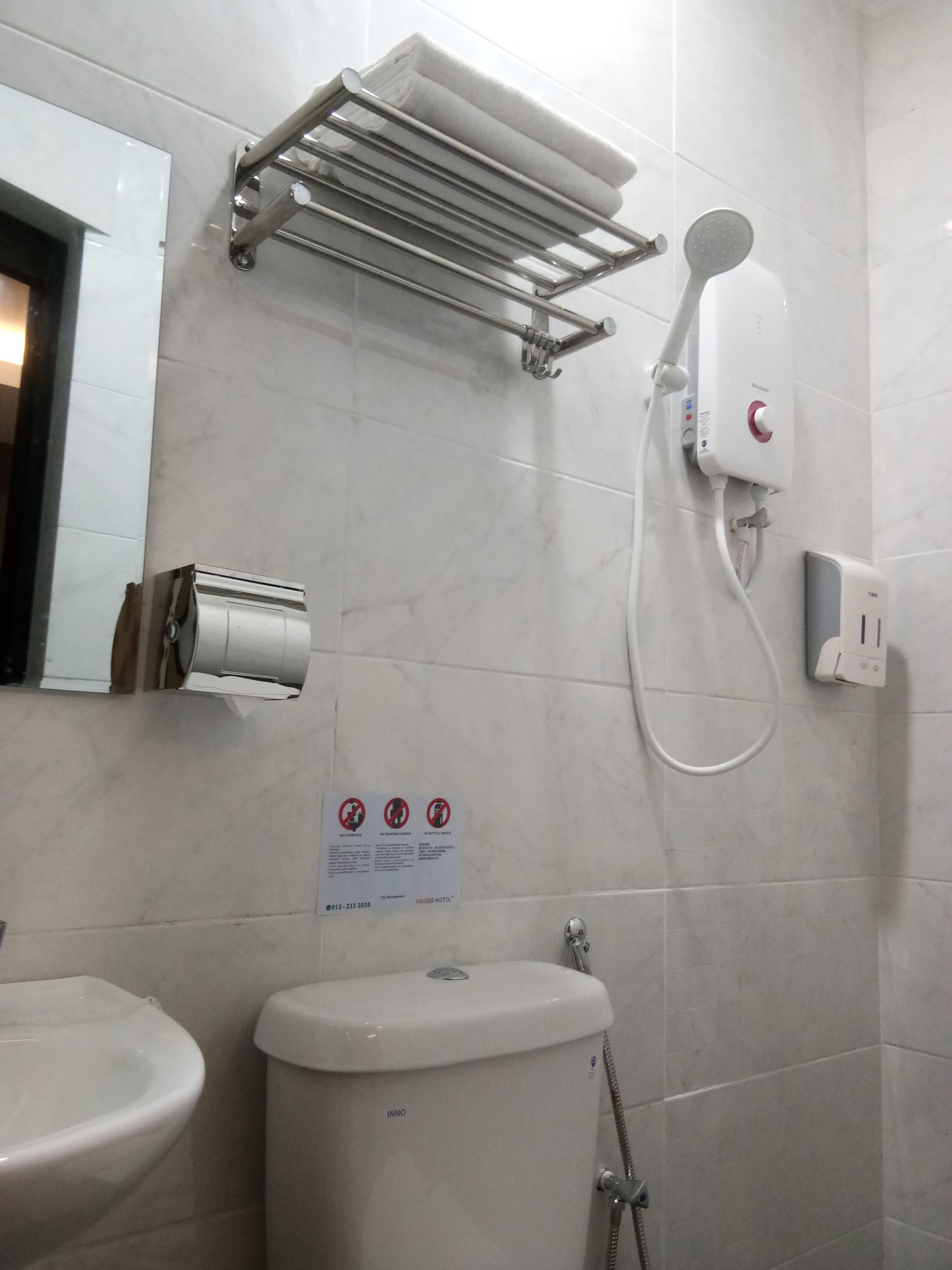 A bathroom with a toilet, sink, towel rack, and a shower with a control panel.