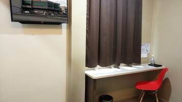 Habitación de hotel con escritorio, una silla roja, televisor montado en la pared y ventana con cortinas.