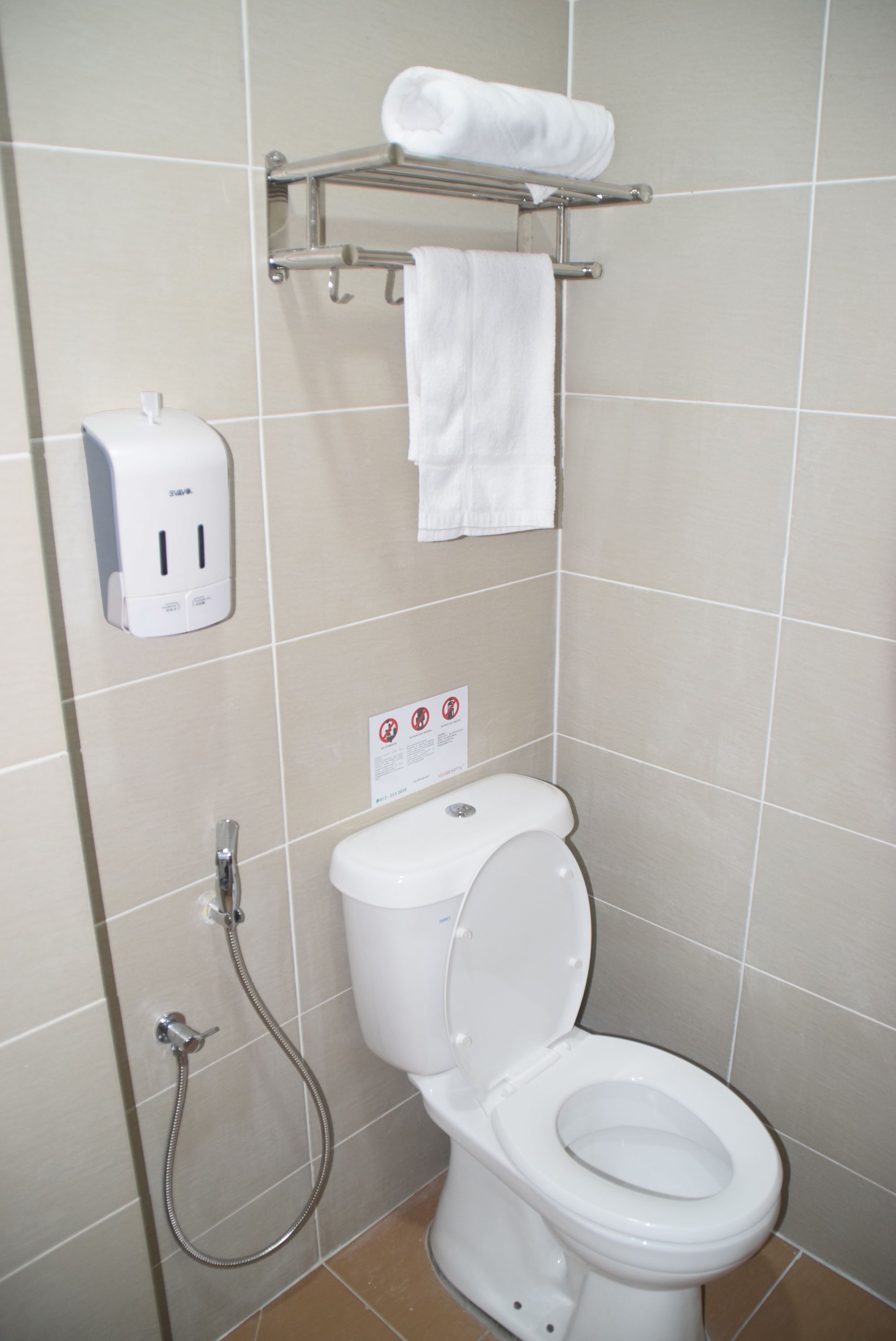 A bathroom with a toilet, a hand dryer, a towel rack with a towel, and a sign on the wall.