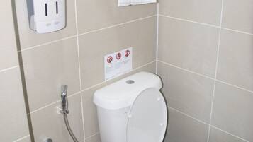A bathroom with a toilet, a hand dryer, a towel rack with a towel, and a sign on the wall.