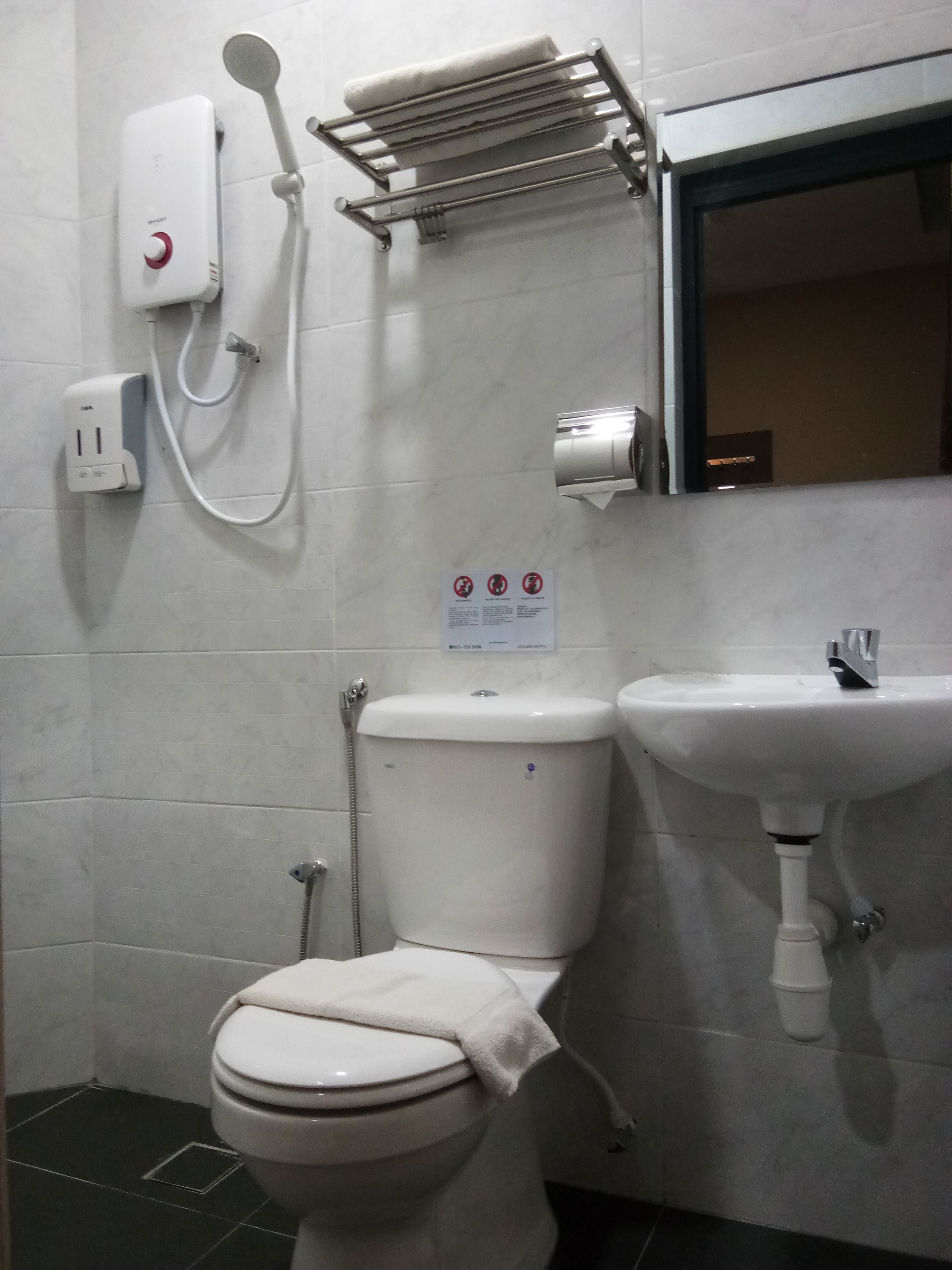 Un baño con inodoro, lavamanos, toallero, cabezal de ducha y secador de manos.