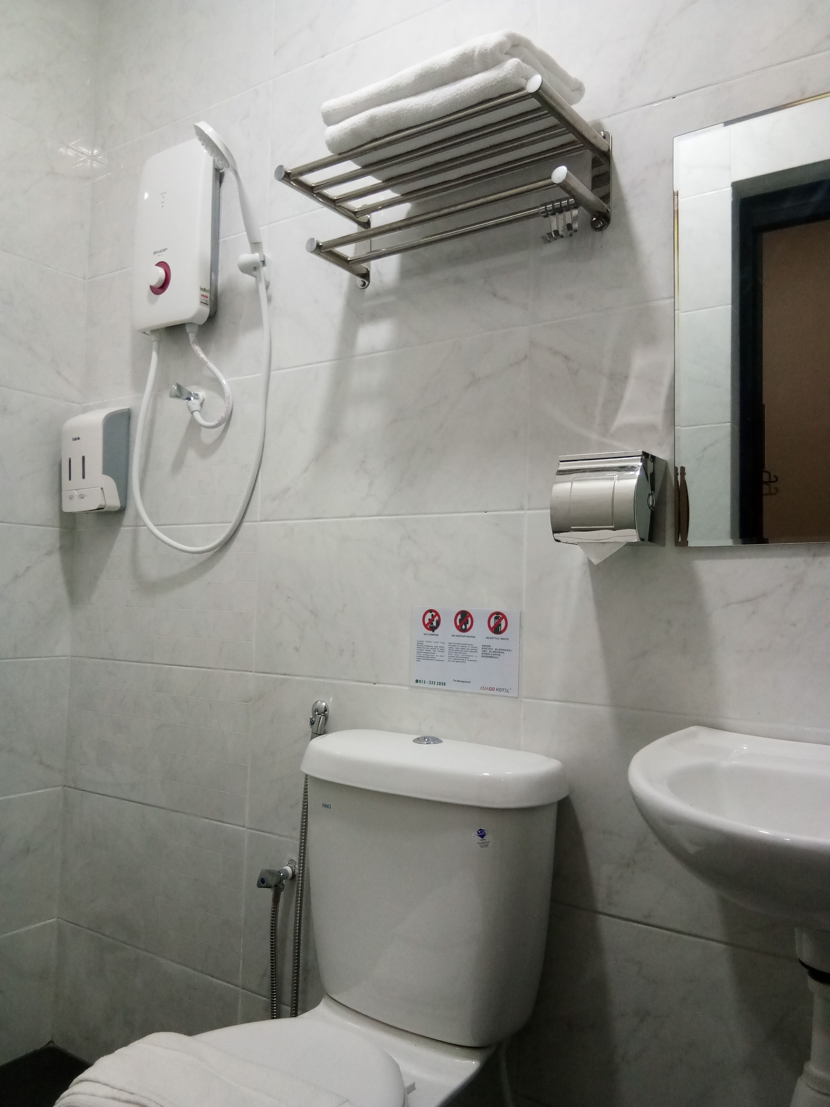 A bathroom with a toilet, a sink, a towel rack, a hand dryer, and a sign with no smoking symbols.