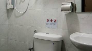 A bathroom with a toilet, a sink, a towel rack, a hand dryer, and a sign with no smoking symbols.