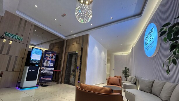 Un vestíbulo de hotel con una recepción, un quiosco de información digital, una araña de cristal y zonas de estar.