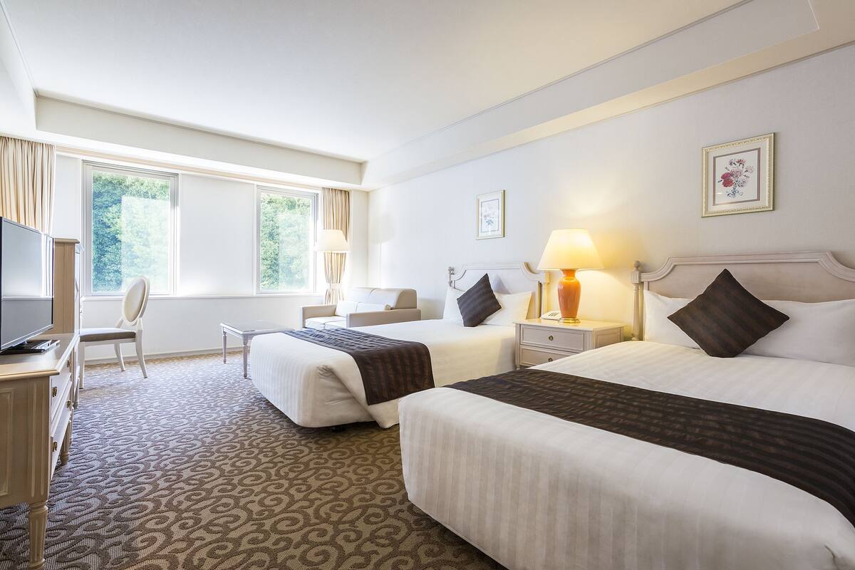 Una camera d'albergo con due letti, una scrivania, una sedia e un televisore.