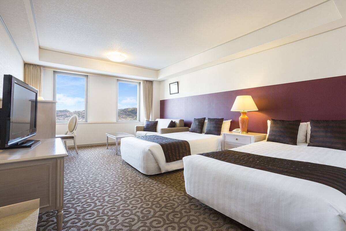 Camera d'albergo con due letti, una scrivania con televisione, una sedia e una finestra con vista.