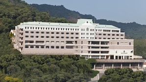 A multi-story hotel with a flat roof, surrounded by dense greenery and hills in the background. - Luke Plaza Hotel (Nagasaki)