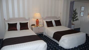A hotel room with two beds, a nightstand with a lamp, a clock, and a potted plant.
