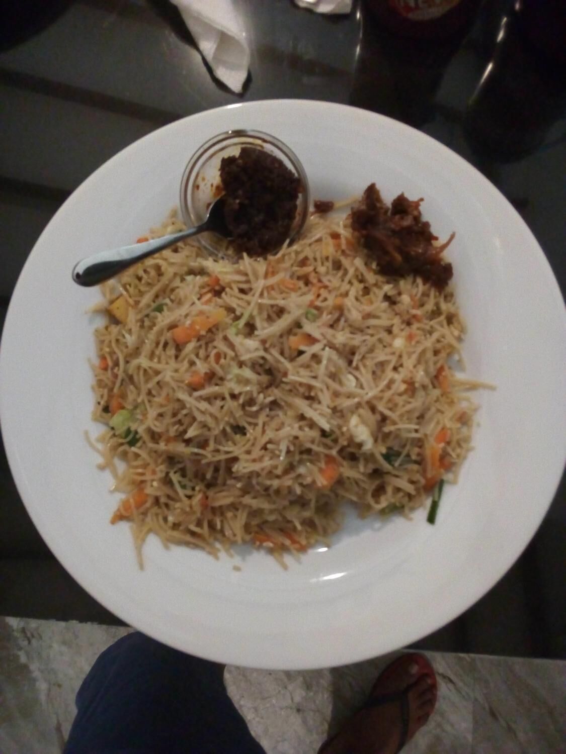 A plate of noodles with vegetables and a small bowl of sauce.